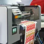High-resolution image depicting the industrial printing process of adhesive labels, showcasing the machinery and label sheet emerging with vibrant red and orange circular designs